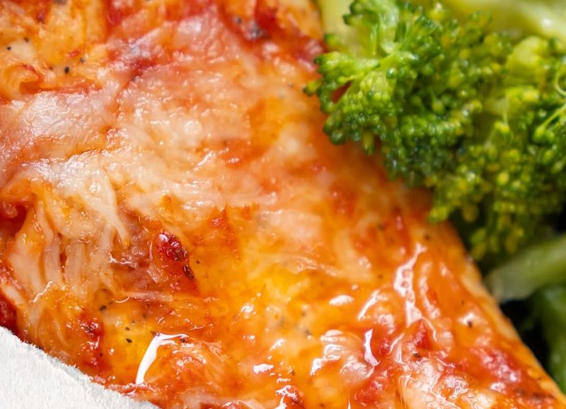 Primer plano de una pechuga de pollo en salsa junto a brócoli recién hecho