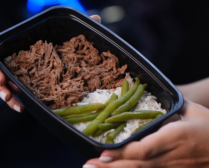 Bandeja con carne de res deshebrada, arroz blanco y habichuelas sostenida con las dos manos